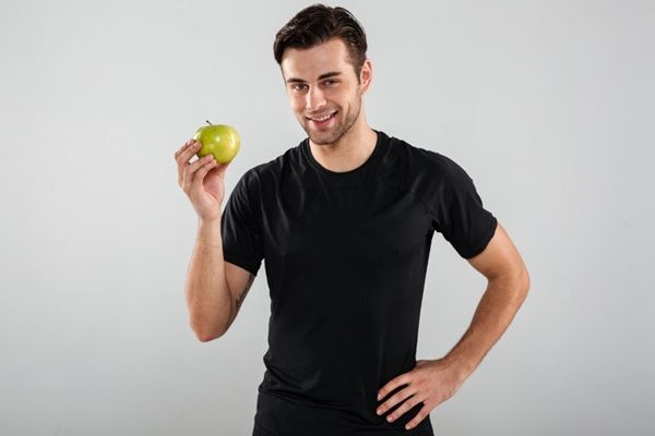 Estética y nutrición - Hombre sosteniendo una manzana, uno de los alimentos antioxidantes más importantes para una piel saludable