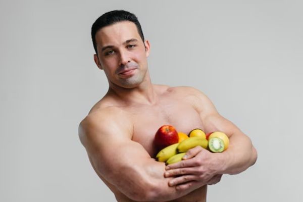 Estética y nutrición - Hombre con una estética fuerte y saludable sosteniendo diversas frutas como fuente de nutricosmética para obtener vitaminas