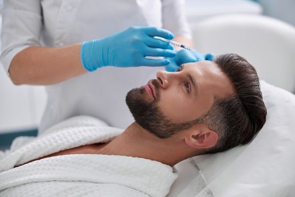 Revitalización facial Madrid - Esteticista aplicando un tratamiento de rejuvenecimiento facial con ácido hialurónico Madrid a un hombre