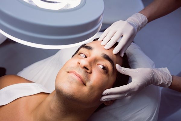 Esteticista aplicando un tratamiento de ácido hialurónico Madrid en el rostro de un paciente masculino