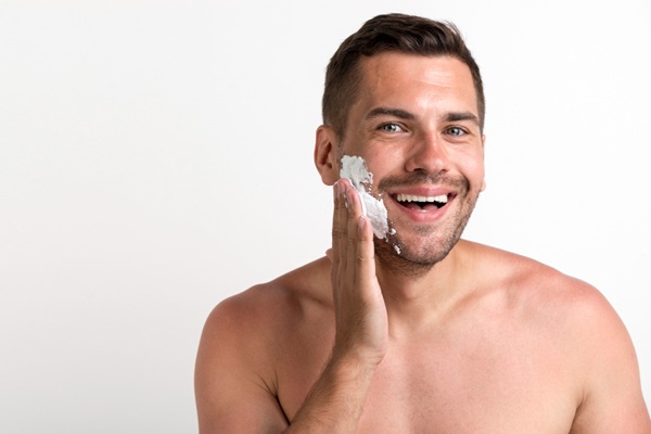 Piel masculina - Hombre feliz aplicándose un skin care con remedios naturales como parte de la rutina diaria de rejuvenecimiento facial