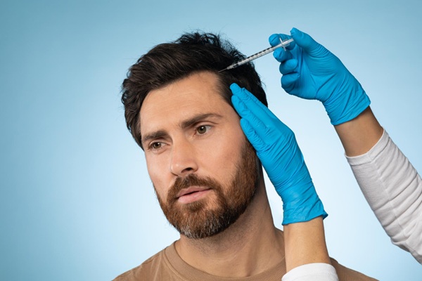 Médico capilar aplicando plasma rico en plaquetas en el cuero cabelludo de un hombre para estimular el crecimiento del cabello